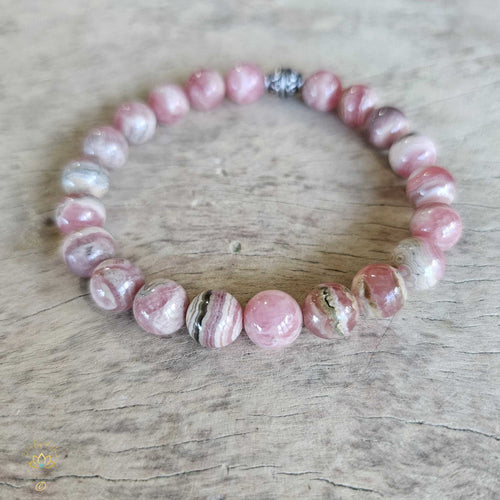 Rhodochrosite bracelet with pink and white striped beads, displayed on a wooden surface.
