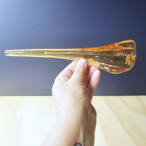 Hand holding a transparent amber-colored glass object against a blurred background
