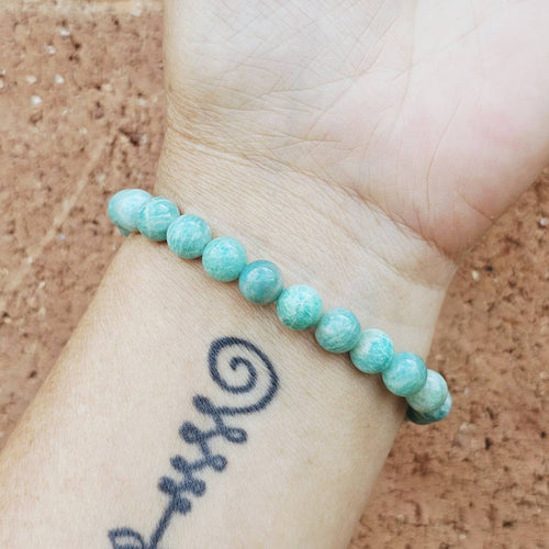 amazonite beaded bracelet on a wrist with a tattoo against a cork background